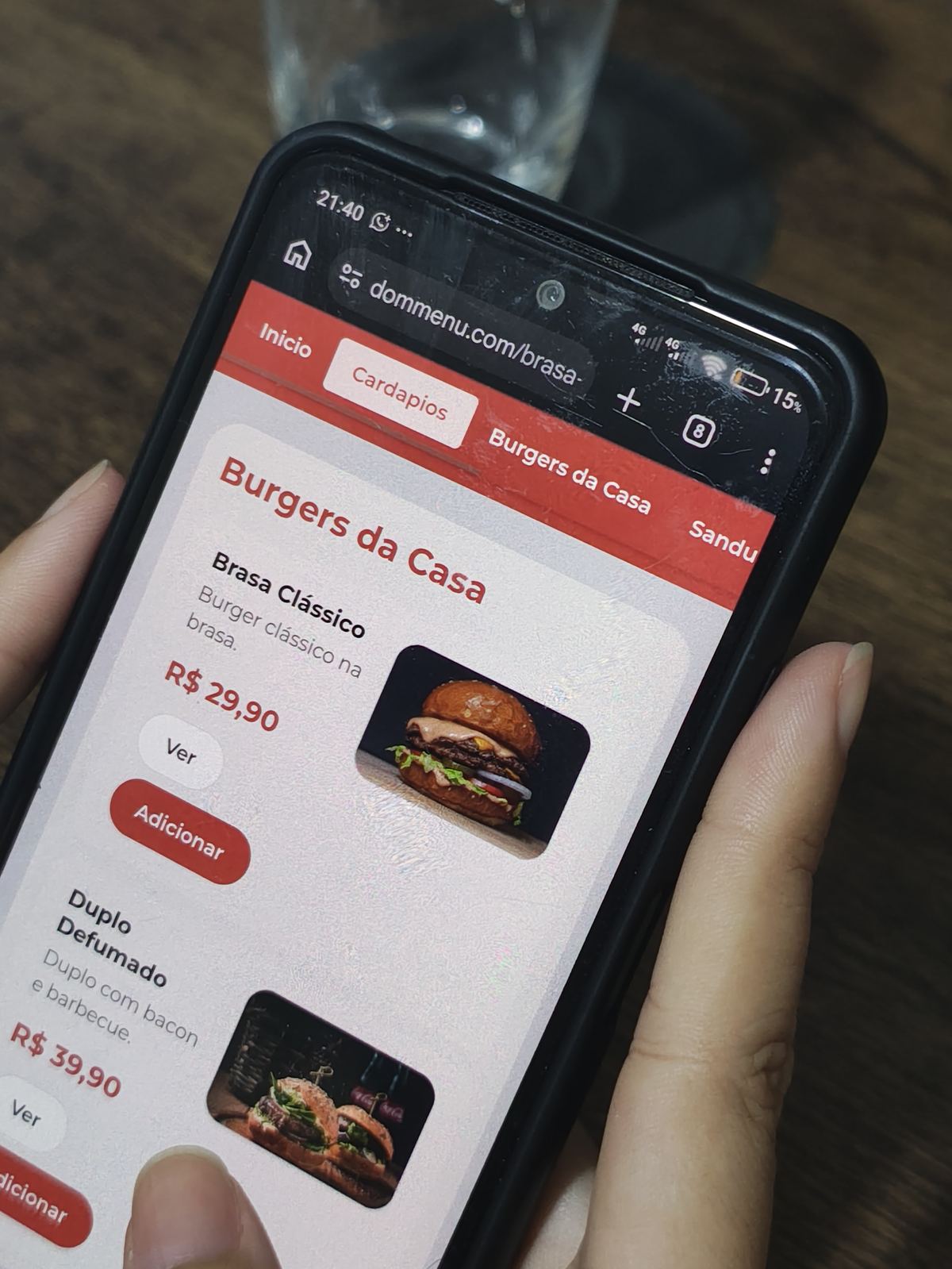 Celular na mesa com o cardápio da Brasa Burger House aberto, mostrando Burgers da Casa e o Brasa Clássico a R$ 29,90